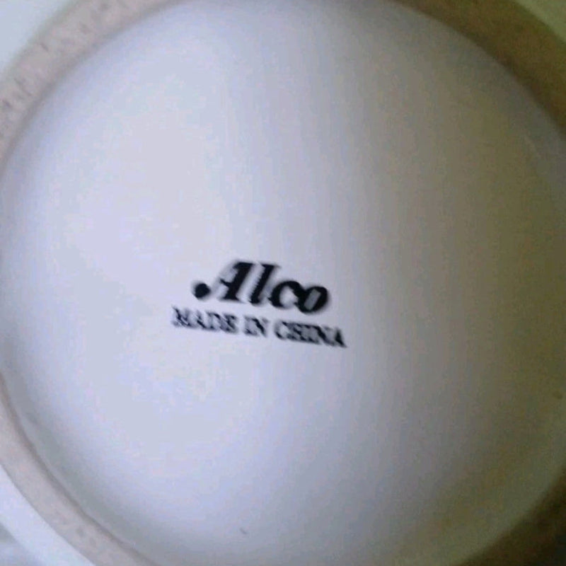 Close-up of a white ceramic item with 'Alco Made in China' text on a white blurry blubackground