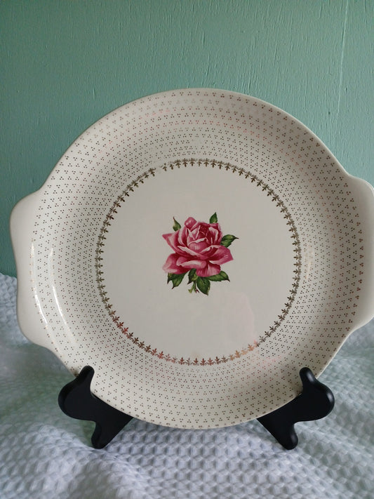 Decorative plate with a pink rose design on a stand against a teal background
