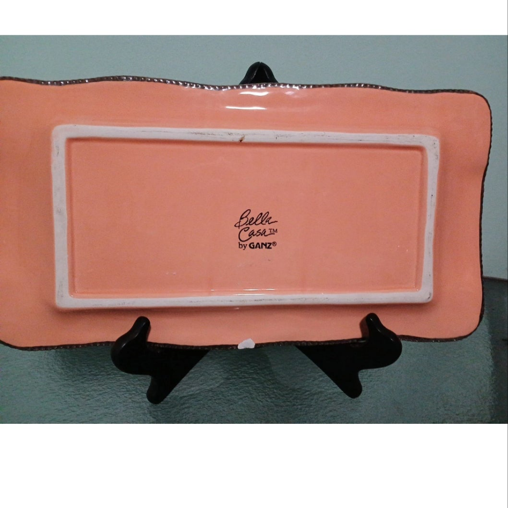 Pink ceramic plate with 'Belle Casa by Ganz' branding on a stand.