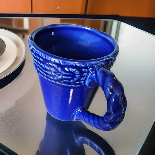 Blue ceramic mug with a unique handle design on a reflective surface.