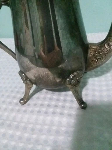 Silver teapot with decorative legs on a textured surface