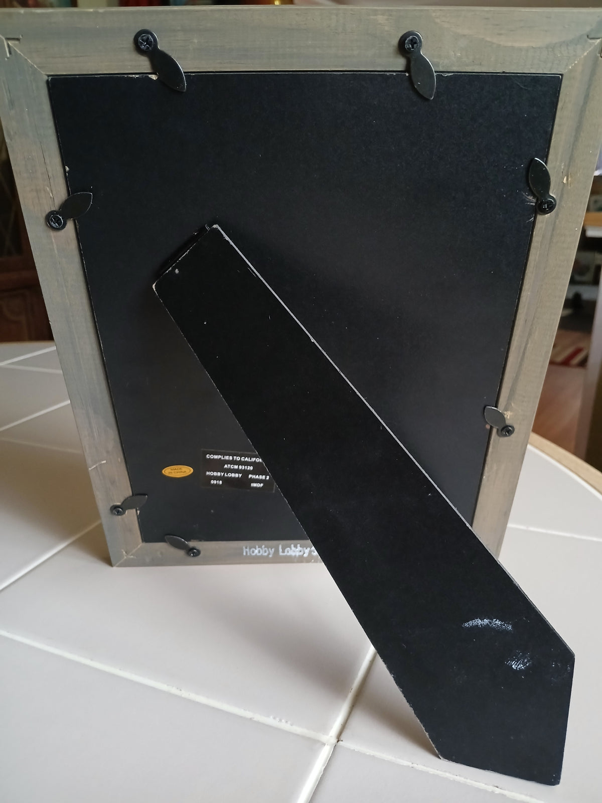 Black metal bracket attached to a wooden frame on a tiled wall.