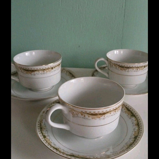 Three white teacups with gold trim on a light surface against a green wall.