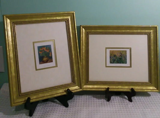 Two gold-framed artworks on stands against a teal wall.