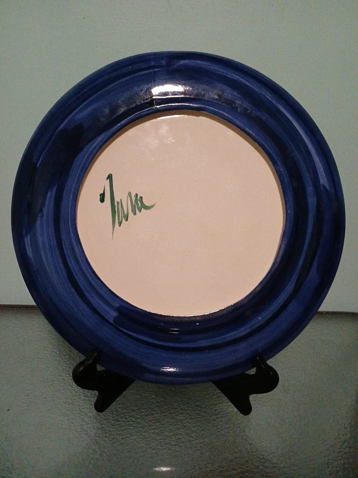 Blue ceramic plate with a signature on a stand against a plain background