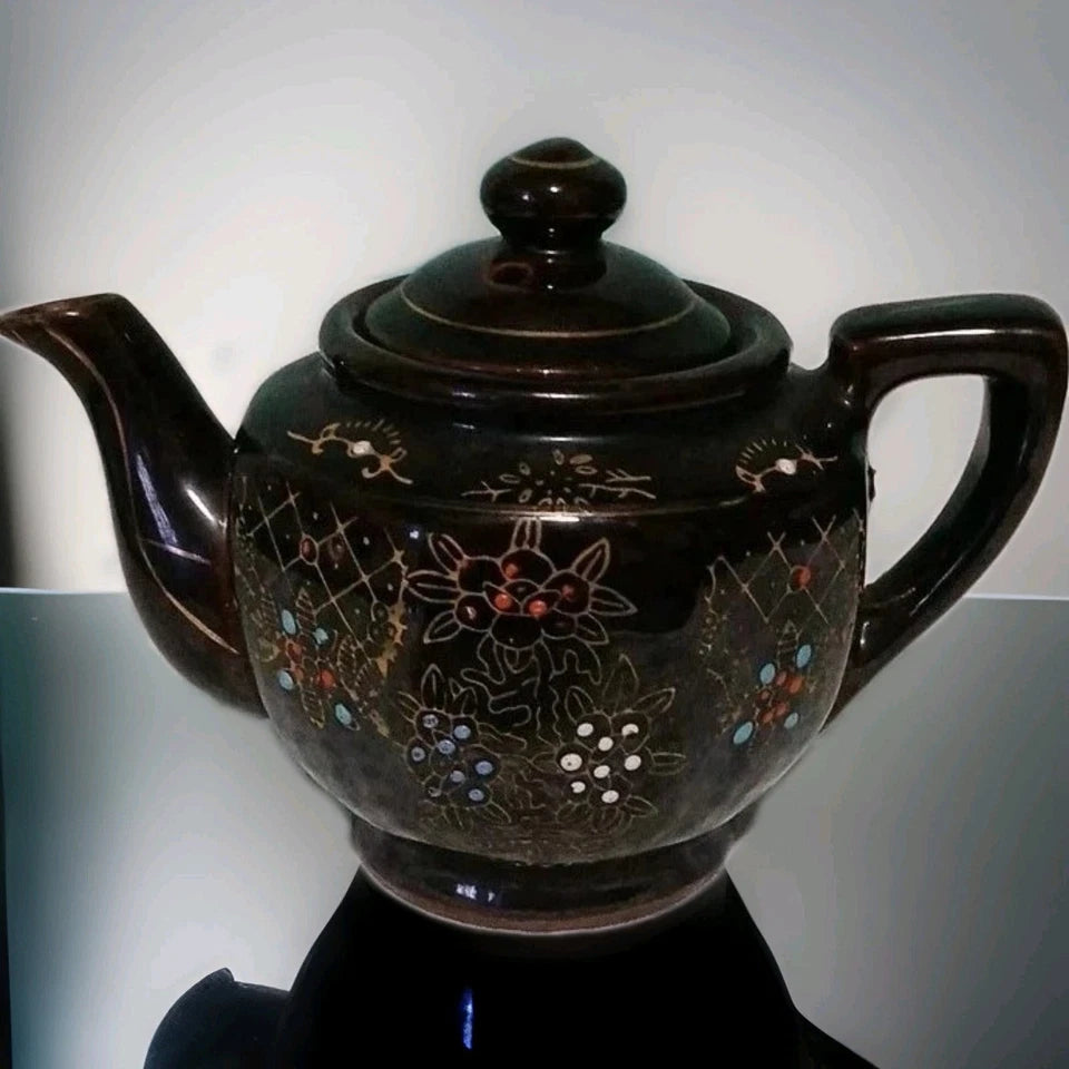 Decorative black teapot with floral patterns on a white background