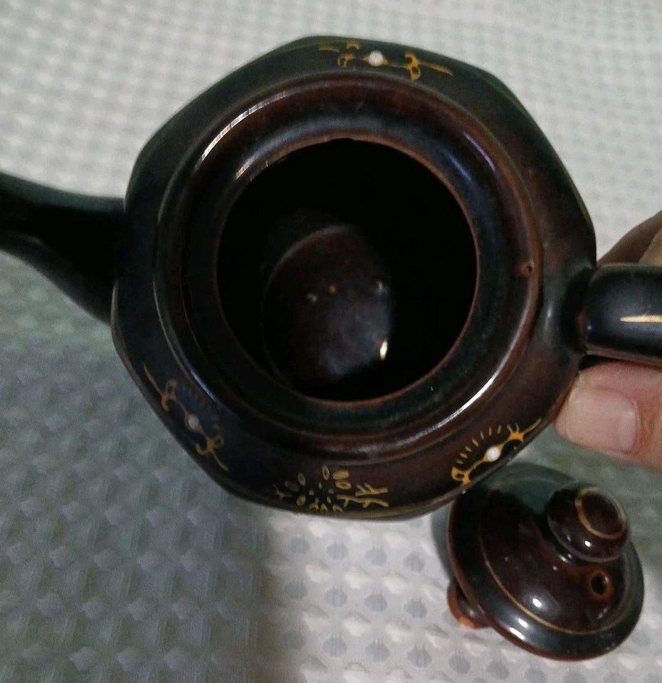 Close-up of a dark brown teapot with gold accents on a textured gray background