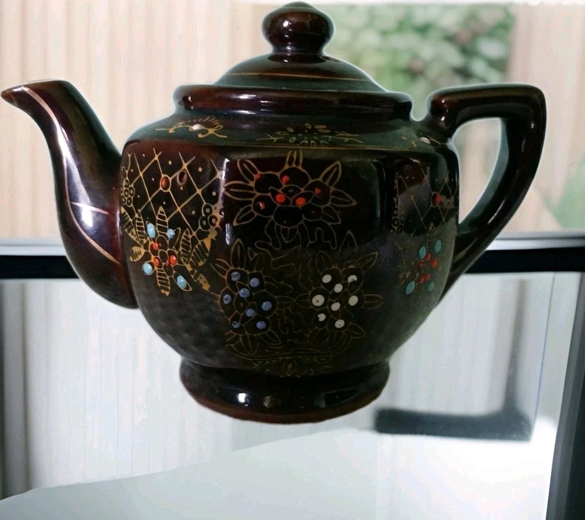 Black ceramic teapot with floral designs on a white surface
